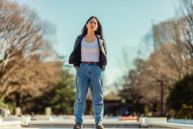 A portrait of a young woman standing alone in a public park on a sunny day.