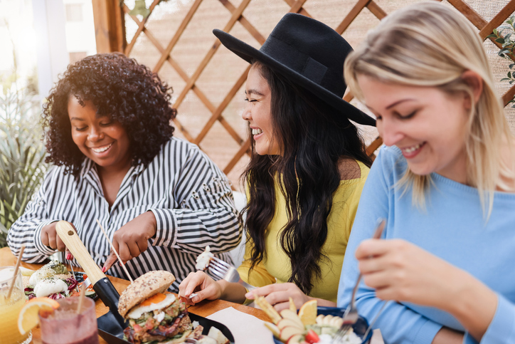 Mature multiracial friends having breakfast outdoors in restaurant - Focus on asian girl face