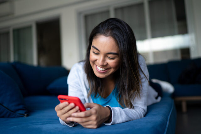 Happy young woman using smartphone at home