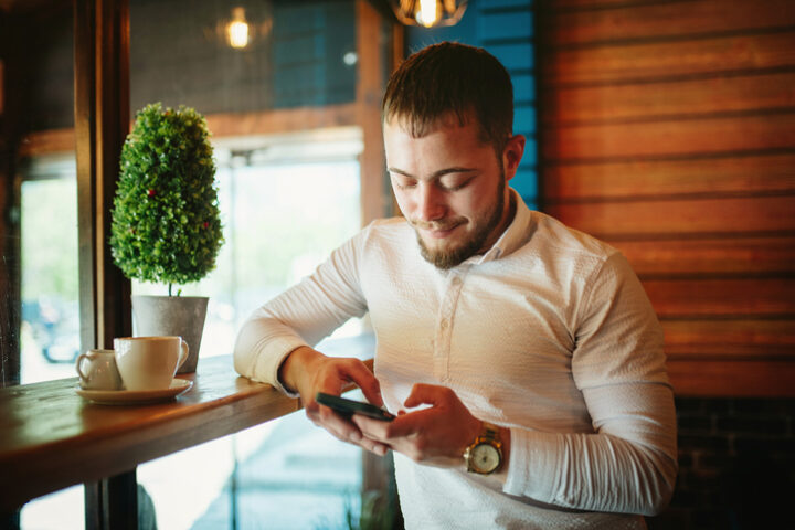 Young man sitting in coffee shop and using a smart phone.
