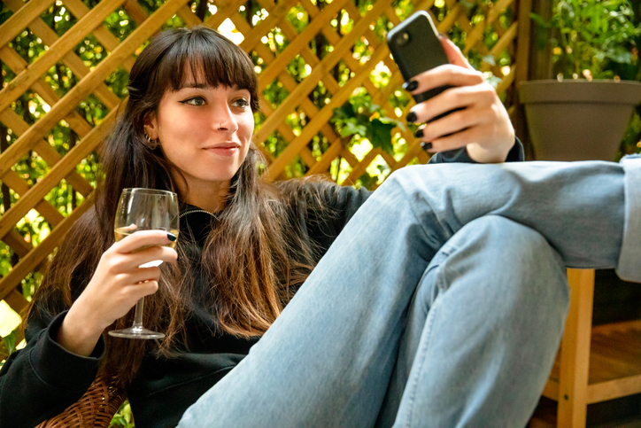 Young woman using smartphone and relaxing with a glass of wine