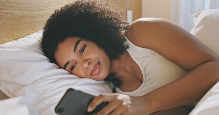 A woman using her phone in bed before sleeping in the evening. Young female chatting on social media lying inside her bedroom at home or house. Lady checking notification browsing internet before nap