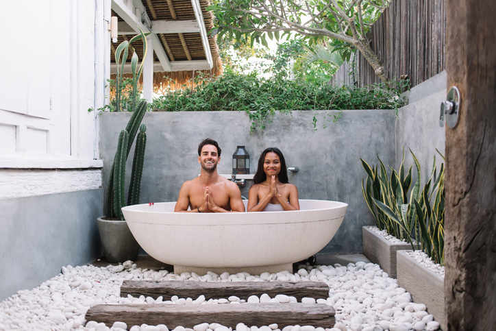 Smiling couple meditating in stone bathtub.