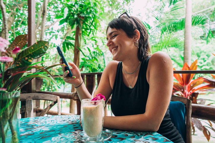 Smiling woman is using phone in an outdoors cafe.
