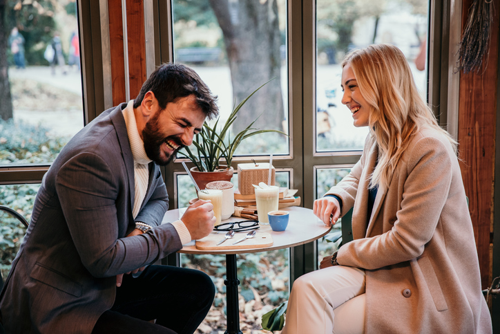 Cheerful elegant dressed man having a conversation with an elegant casual dressed blondie, both drinking a coffee and fresh juice and having a work break.
