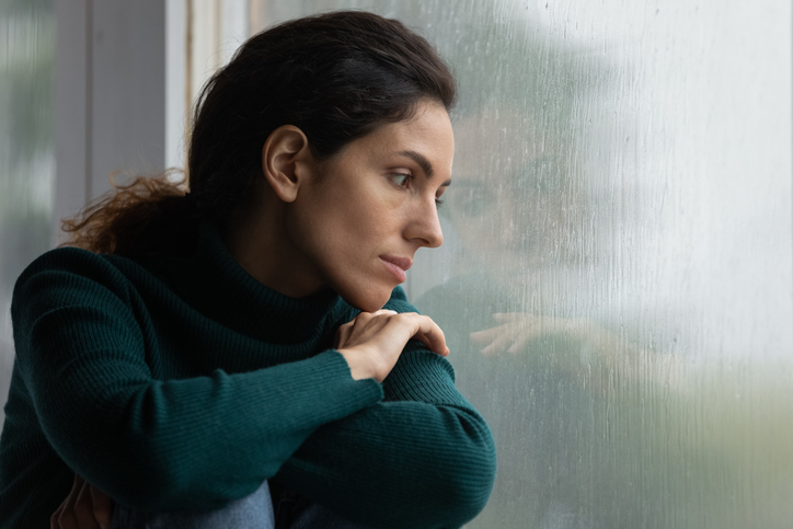 Woman alone looking out a window appearing sad.