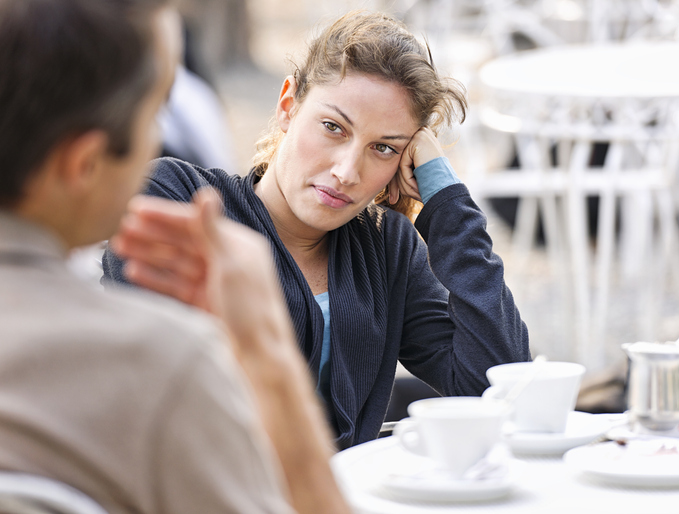 A woman listening to a man (defocussed) talking during a discussion at an outdoor cafe.