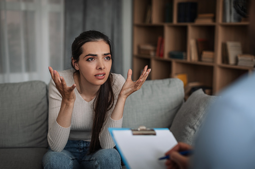Frustrated emotional young woman receiving therapy in consultation with doctor psychologist