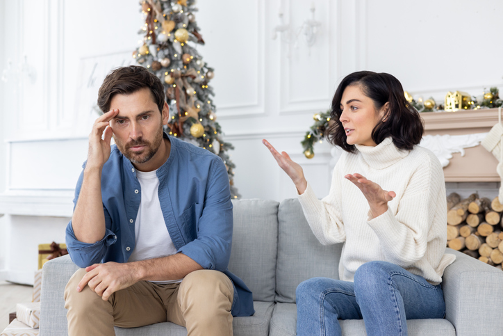 Conflict of a young couple, family on New Year's holidays. A young man and a woman are sitting on the couch and arguing. The wife screams and accuses the husband, the husband holds his head.