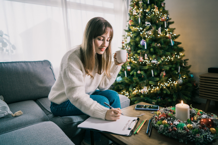 Young Woman with cup is hand writing New year's goals on note paper in new year day. New year resolutions list. Goals, resolutions, plans, action, checklist concept. New Year template, copy space.