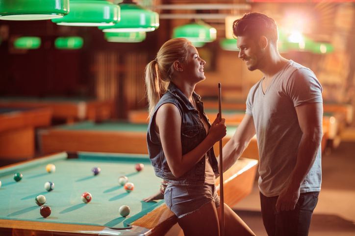 Happy woman enjoying a billiard game while talking to young man, they are both flirting with each other
