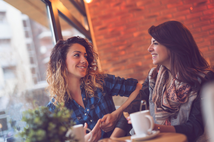 Two beautiful young women sitting in a cafe, drinking coffee and having a pleasant conversation. Focus on the girl on the left