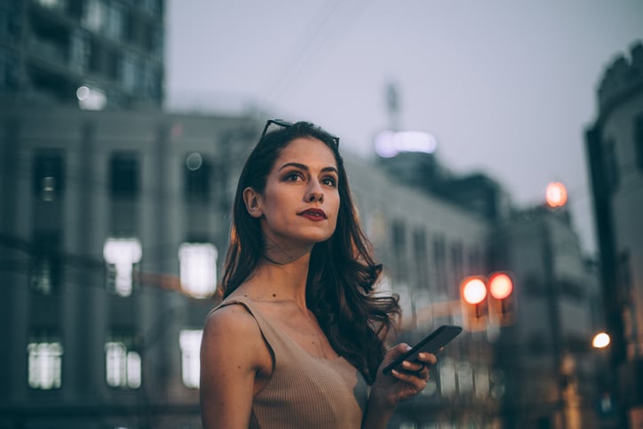 One woman, standing outdoors alone, using smart phone.