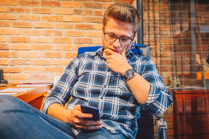 Young business man looking worried while reading text messages and texting with his smartphone.
