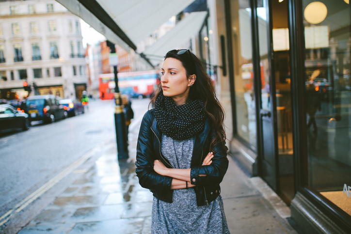 Vintage toned portrait of a young beautiful brunette woman, walking in London, by the shops in Soho district. She is wearing casual Autumn clothes, black leather jacket, gray tunic and a scarf.