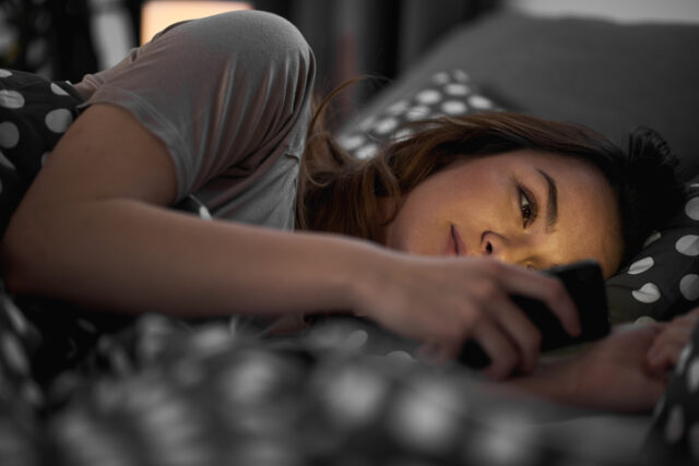 Girl using smart phone and lying down in bed late at night
