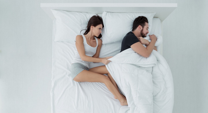 Couple sleeping in bed, the man is stealing the duvet and the woman is angry and freezing