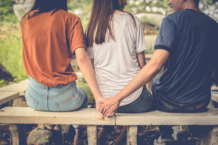 Boyfriend and another woman grab hands from behind together without sight of his girlfriend.. Paramour and divorce concept. Social problem and cheating couples theme. Teen adult and University theme.