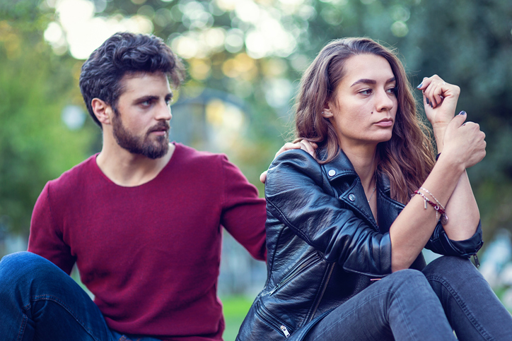 Young irritated woman ignoring her boyfriend while sitting outdoors in the park
