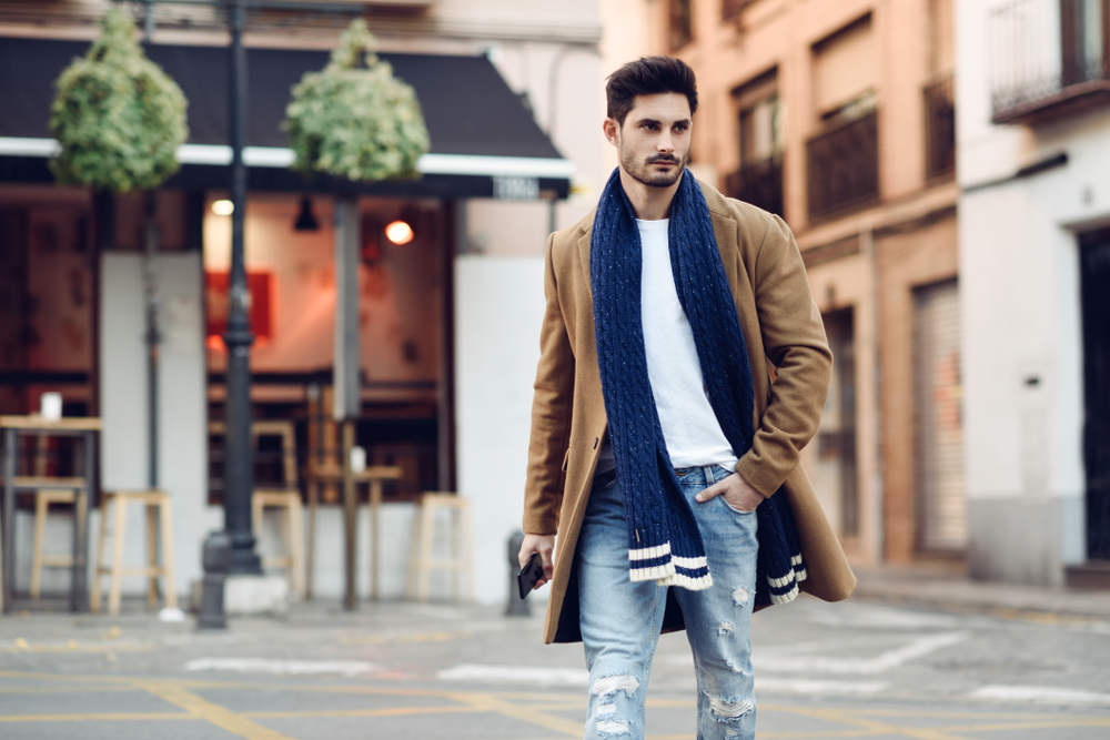 Young man wearing winter jacket with a smartphone in his hand crossing the road