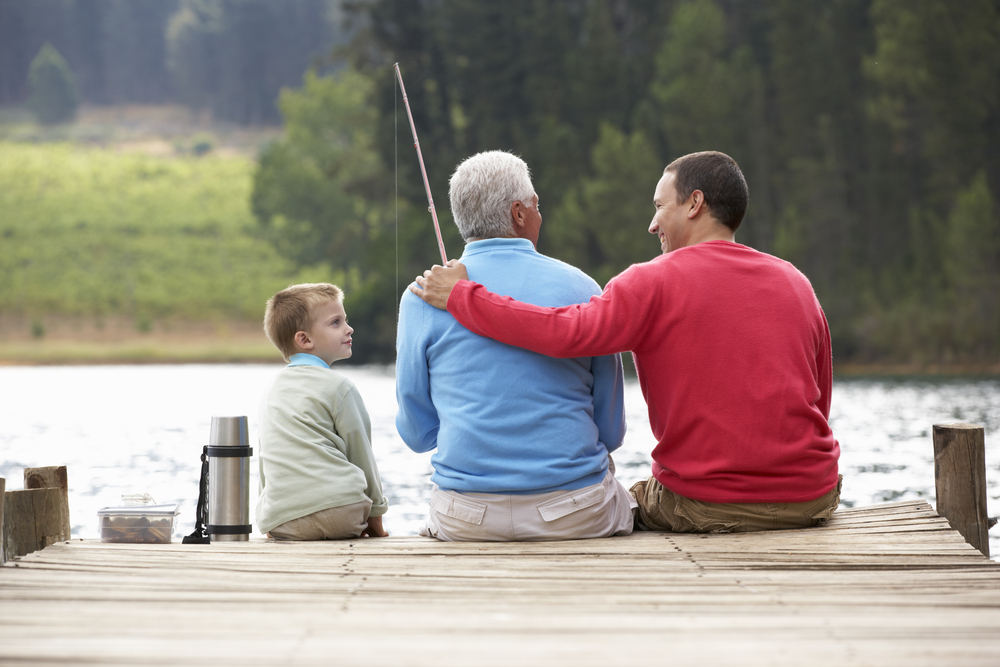Three generations of men sitting by the river bank, grandfather, son and grandson
