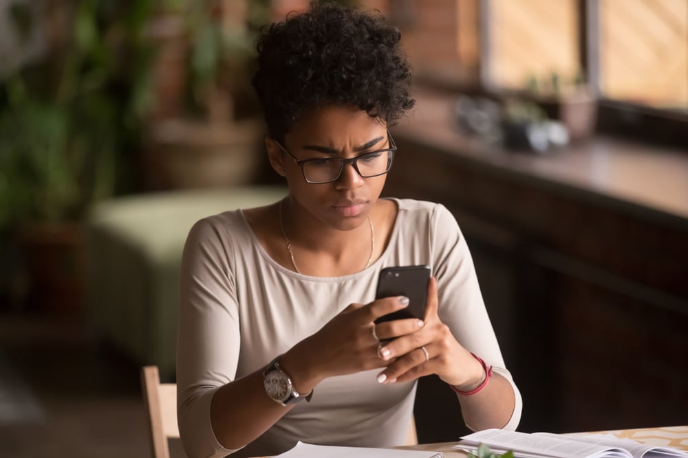 Upset confused young woman looking at her phone