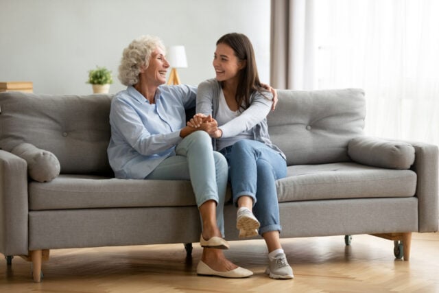 A happy adult granddaughter sitting on the living room sofa with her grandmother
