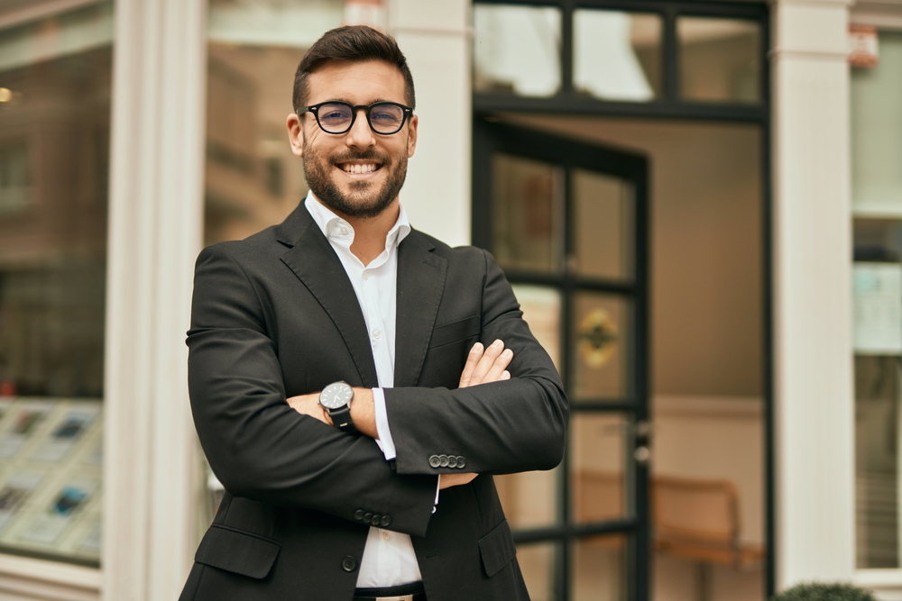 A young smiling businessman in suit with arms folded
