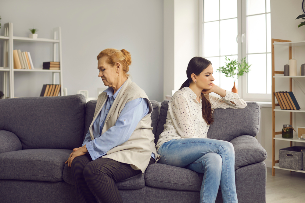 An ofended mother and daughter sitting on the couch with their backs turned to each other