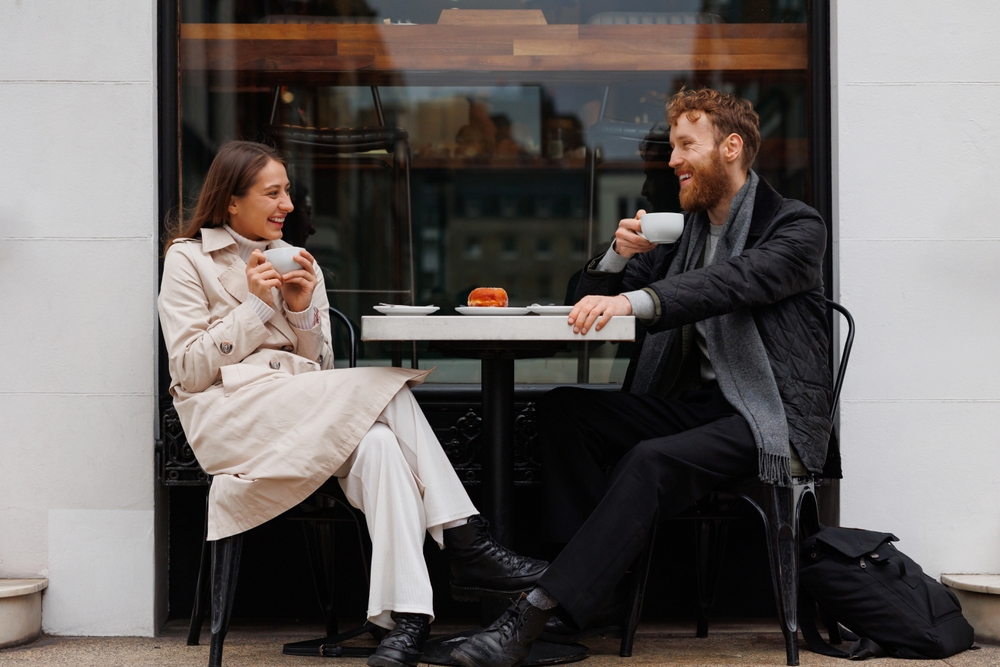 Happy couple at a cafe drinking coffee and laughing at a joke.