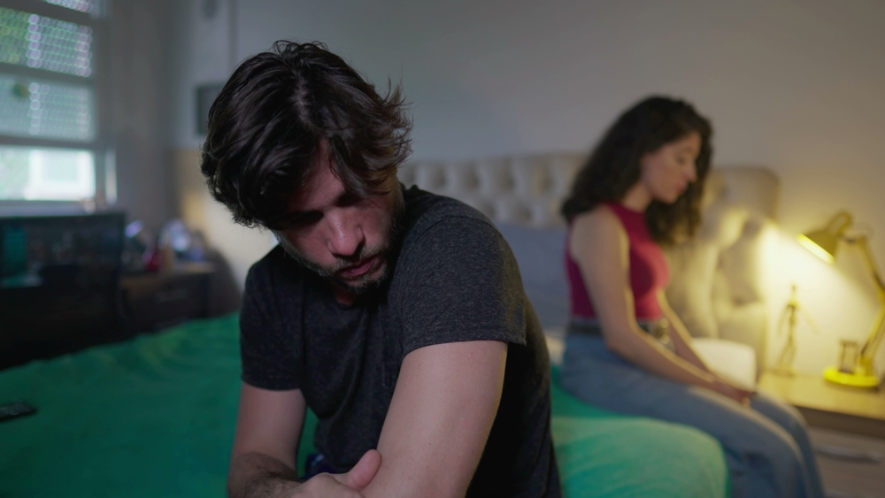 An unhappy couple sitting apart from each other in bed, feeling sad