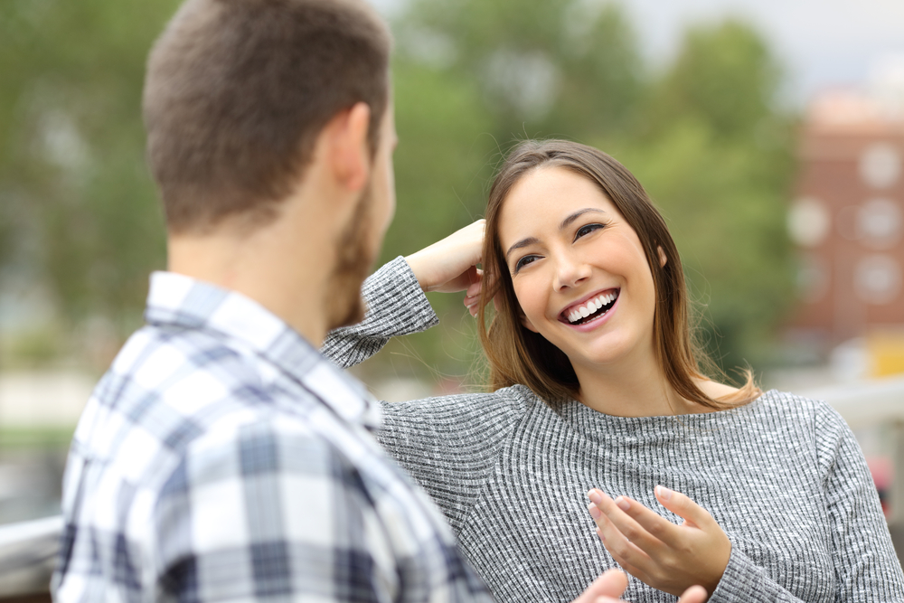 A young couple having a conversation and smiling at each other on a park bench