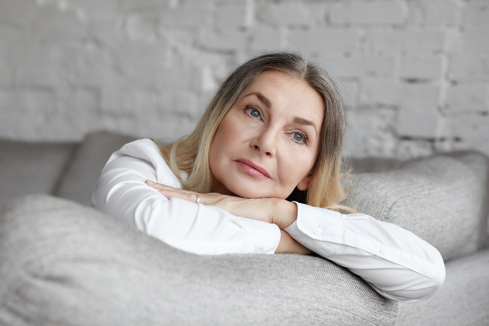 An attractive middle age woman resting her head on her arms on the couch, lost in thoughts