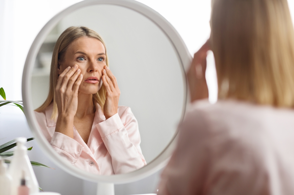 A woman looking into a mirror with her hands on her cheeks