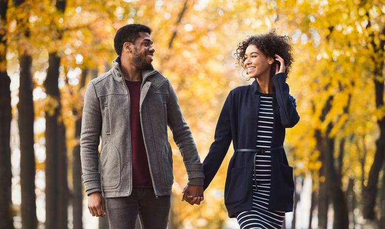 African-american couple in love holding hands and walking through park on sunny autumn day