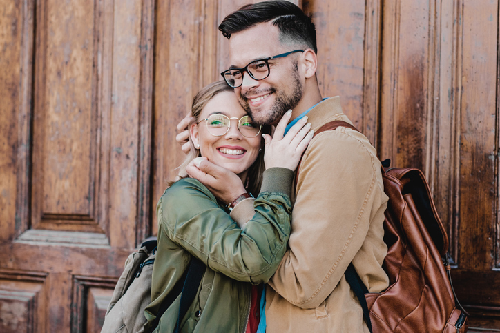A young couple with backpacks hugging while looking away