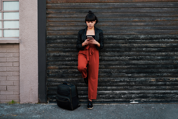Shot of a young woman using her mobile phone while standing in front of a garage door in the city