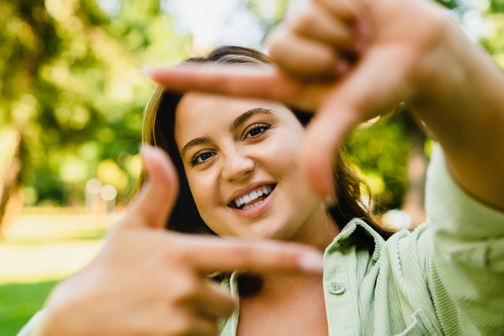 Caucasian young smiling woman posing looking at camera on smart phone while walking in park, doing selfie photo image