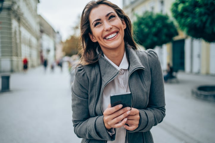 Beautiful young woman walking on the city street and using a smartphone. Shot of an attractive young woman using her cellphone while walking outdoors.