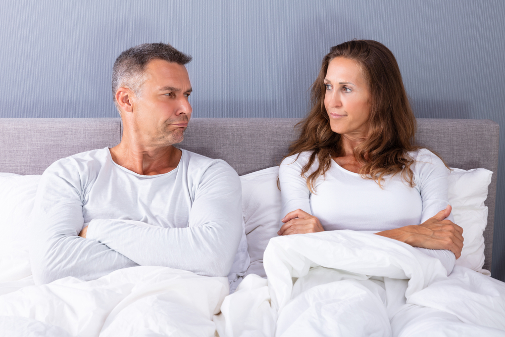 A sad middle age mature couple sitting up in bed