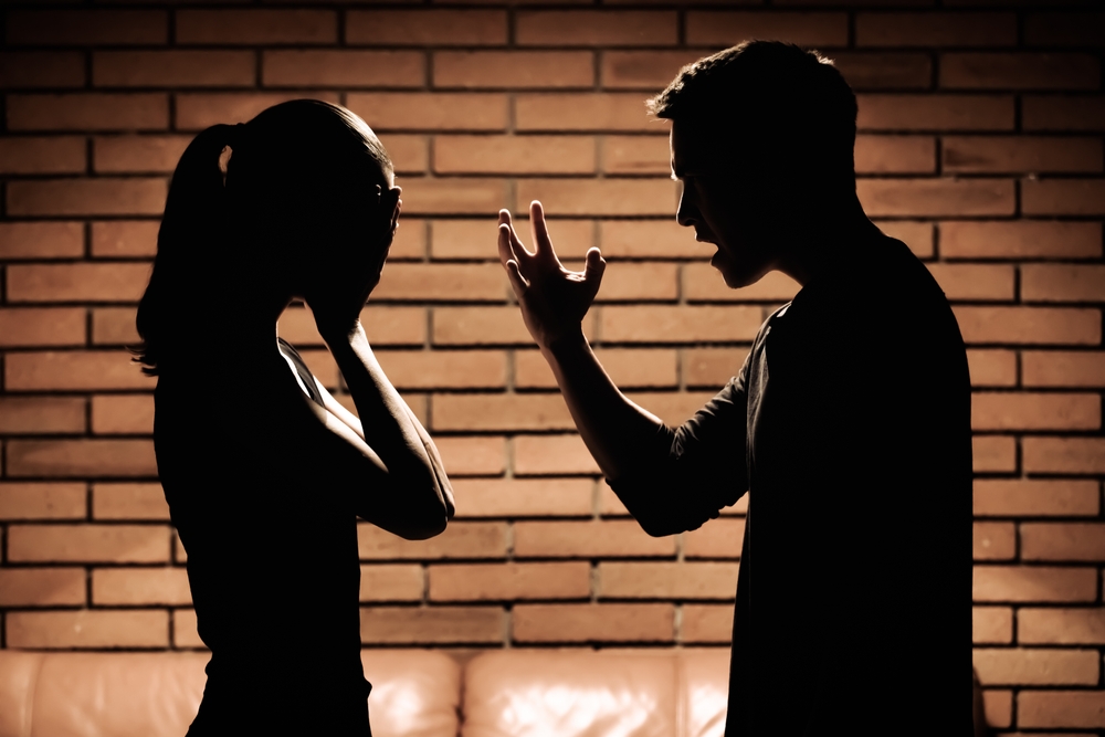 A man screaming and verbally insulting his girlfriend in the dark, she stands there quiet and covers her face with her hands