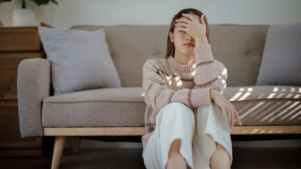 A sad woman sitting on the ground of her living room