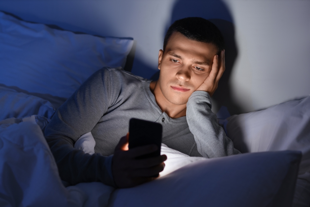 Young man sitting alone in the dark on his phone.