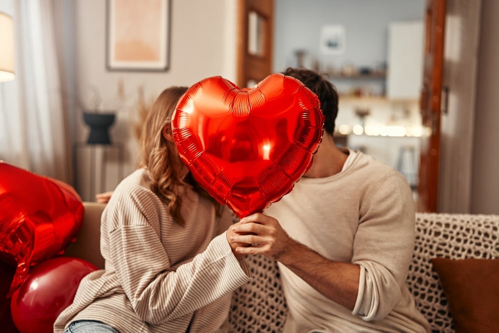 Couple in love kissing behind a red heart balloon.