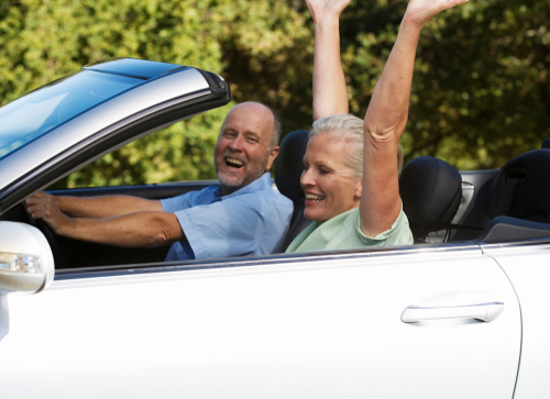 A retired senior couple enjoying a ride in a convertible with the top down