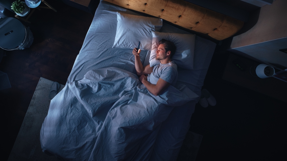 A man laying awake in bed on his phone.