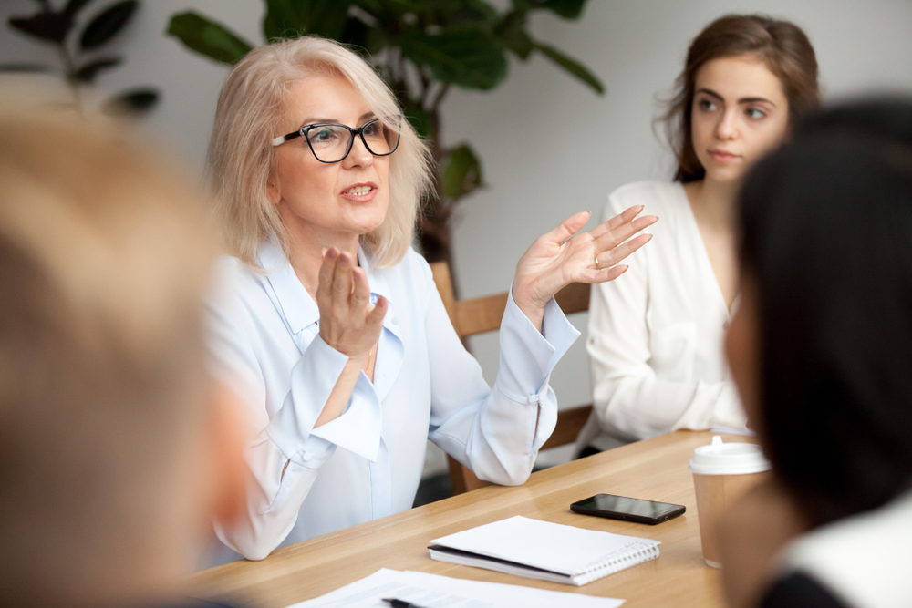 An older mature woman speaking in a business meeting with other work colleagues