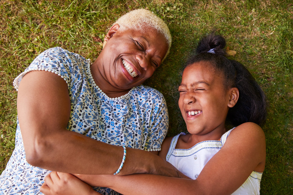 A grandmother and her granddaughter lying on the grass and laughing together.