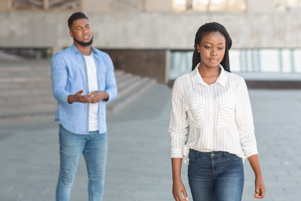 A woman walking away from a man, the man is begging her to come back