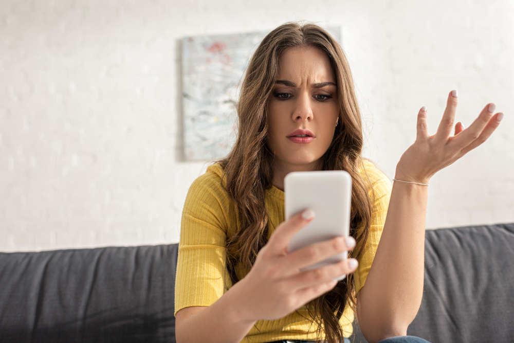 A confused upset young woman looking at her phone